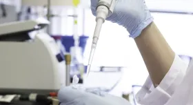 Gloved hands work with a pipette and lab equipment.