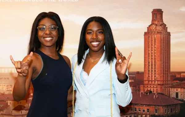 Two female students giving the hook 'em sign.